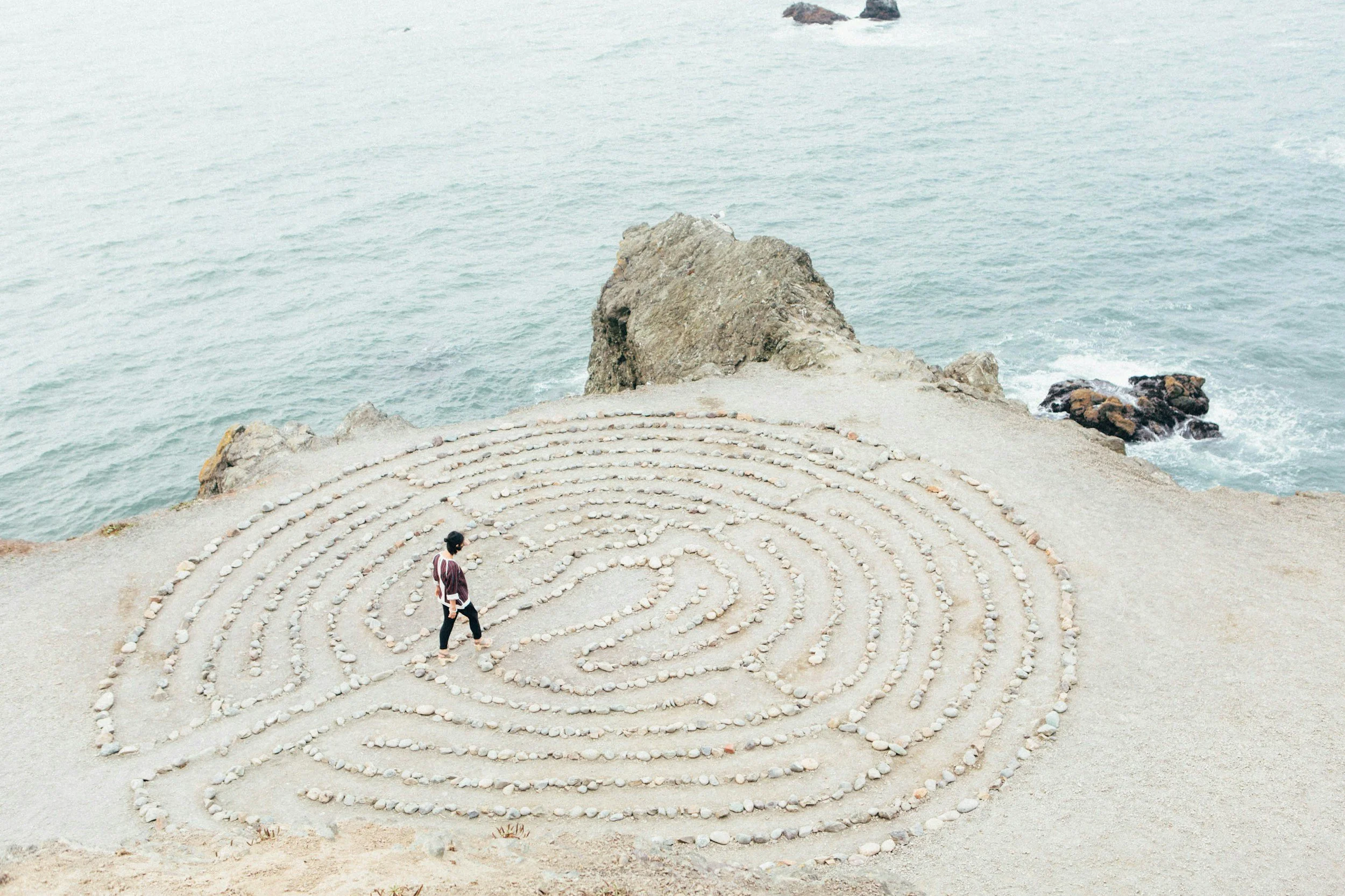 Solo traveler walking through a labyrinth near the ocean, symbolizing mindfulness and self-discovery during travel, with Greether providing safe and empowering experiences for women