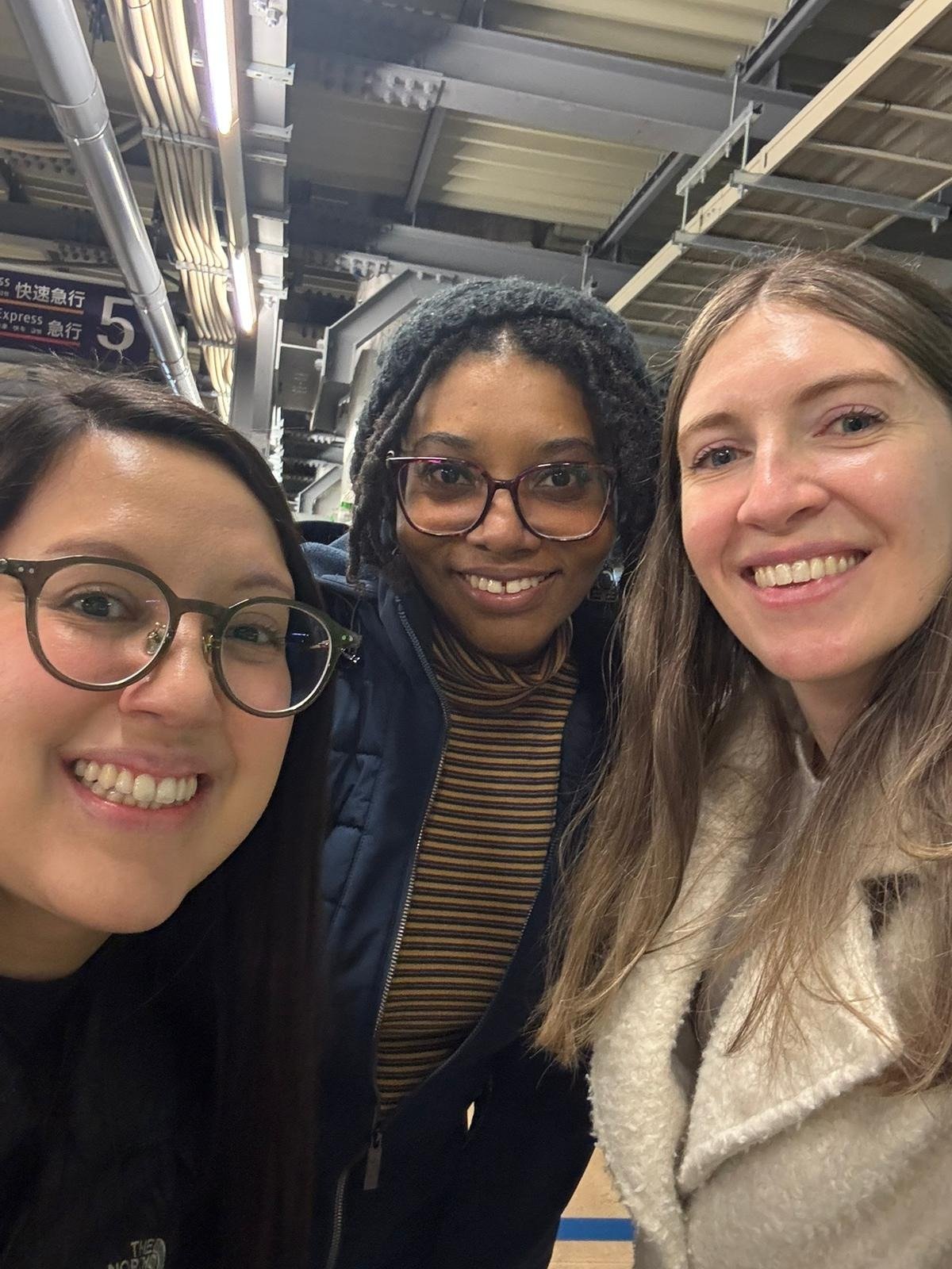Two women traveling together, Kaylee and Easter, with their Greeter Jess on a Tokyo train platform